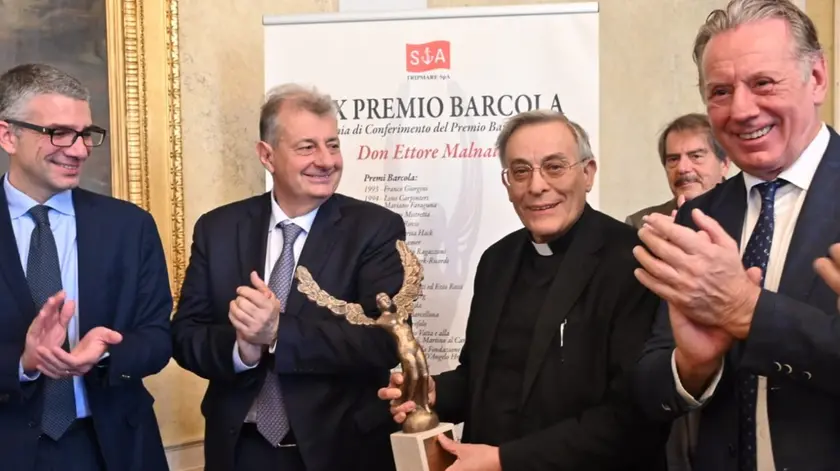 Don Malnati al centro con il premio e alle due estremità gli assessori Roberti e Scoccimarro