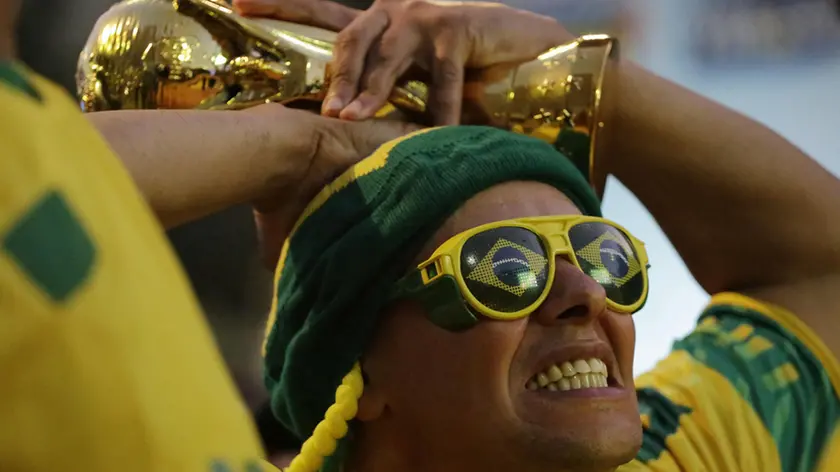 A Brazilian soccer fan decked out in the national soccer team's colors, reacts as he holds onto a replica of the World Cup trophy while watching the game between Brazil and Croatia on a giant screen during the FIFA Fan Fest in Sao Paulo, Brazil, Thursday, June 12, 2014. Brazil and Croatia were tied at halftime of the international soccer tournament opener after Neymar scored the second goal of the match. (AP Photo/Nelson Antoine)