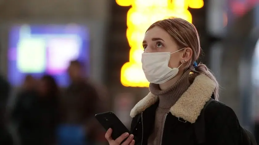 Una ragazza osserva delusa il tabellone dei voli di un aeroporto