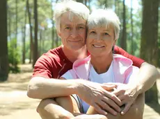 Senior couple in sportswear sitting in wood, man embracing woman, smiling, front view, portrait