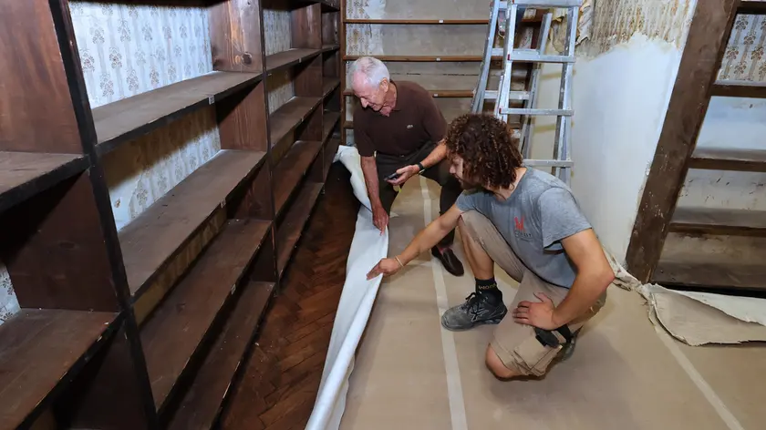 Gli artigiani che stanno lavorando al restauro della libreria scoprono il parquet appena sistemato. Nel pezzo la sala con il pavimento a vista e le vecchie scaffalature: restano da sistemare soffitto e parati. Foto Andrea Lasorte