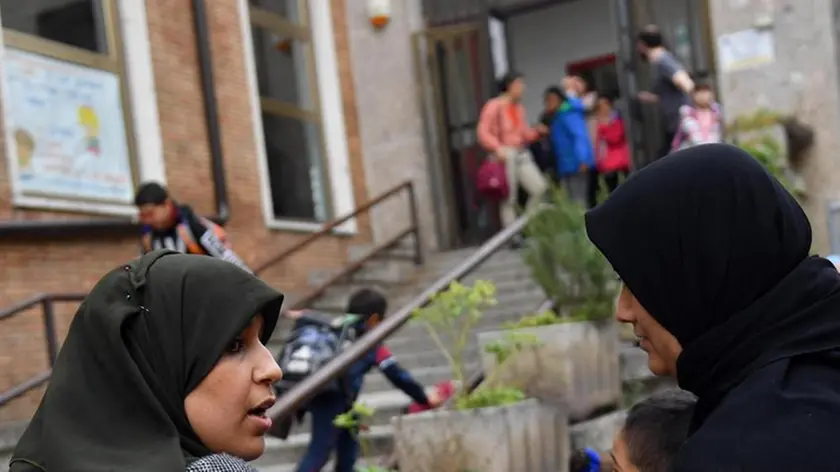 Due madri discutono in attesa dell'uscita dei figli al termine delle lezioni dalla Scuola Primaria S. F. Cabrini a Lodi, 16 ottobre 2018. Dopo le polemiche suscitate dalla decisione del Comune di sospendere la mensa ai bambini stranieri le cui famiglie non fossero in grado di dimostrare il diritto all'esenzione dal contributo, un nuovo caso è scoppiato a Trieste la cui giunta ha approvato un nuovo regolamento per le scuole d'infanzia che pone un tetto del 30% per gli alunni stranieri. ANSA/DANIEL DAL ZENNARO