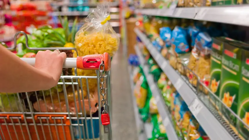 Un carrello pieno tra gli scaffali di un supermercato