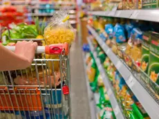 Un carrello pieno tra gli scaffali di un supermercato