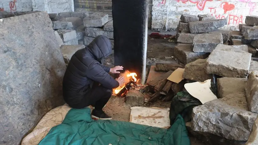 Un migrante si scalda nei magazzini del Porto Vecchio. Foto di Andrea Lasorte