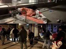 In alto un migrante che riposa nei pressi della stazione e alcuni dei richiedenti asilo invitati ad andare via dal porticato di Selva Arredamenti nelle immagini postate da Cisint