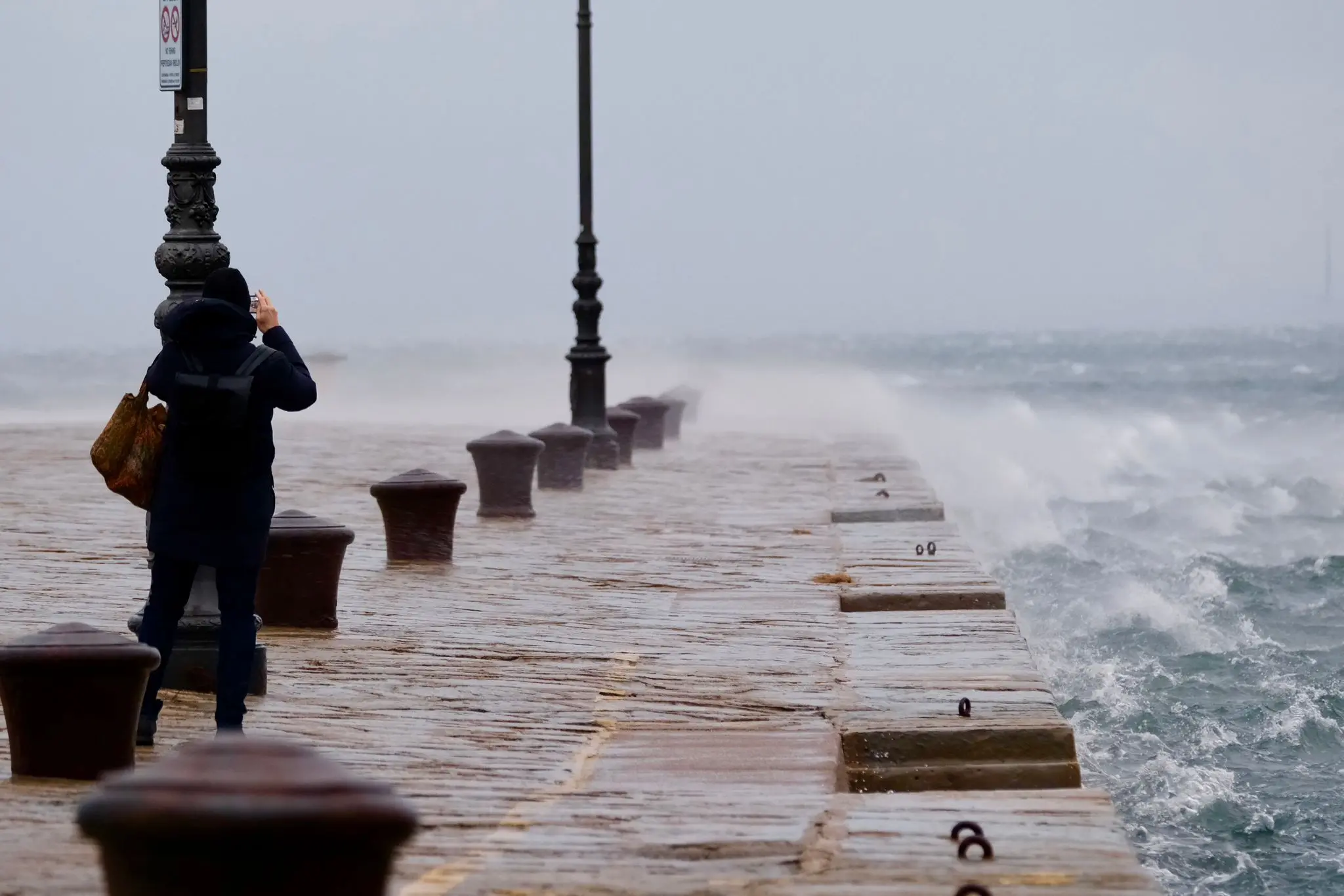 Il molo Audace bagnato dalle onde provocate dalla bora il giorno della vigilia di Natale mentre una coraggiosa immortala il paesaggio. Foto Silvano