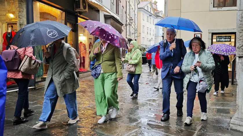 Un gruppo di turisti si ripara dalla pioggia in via San Sebastiano a Trieste (foto Andrea Lasorte)