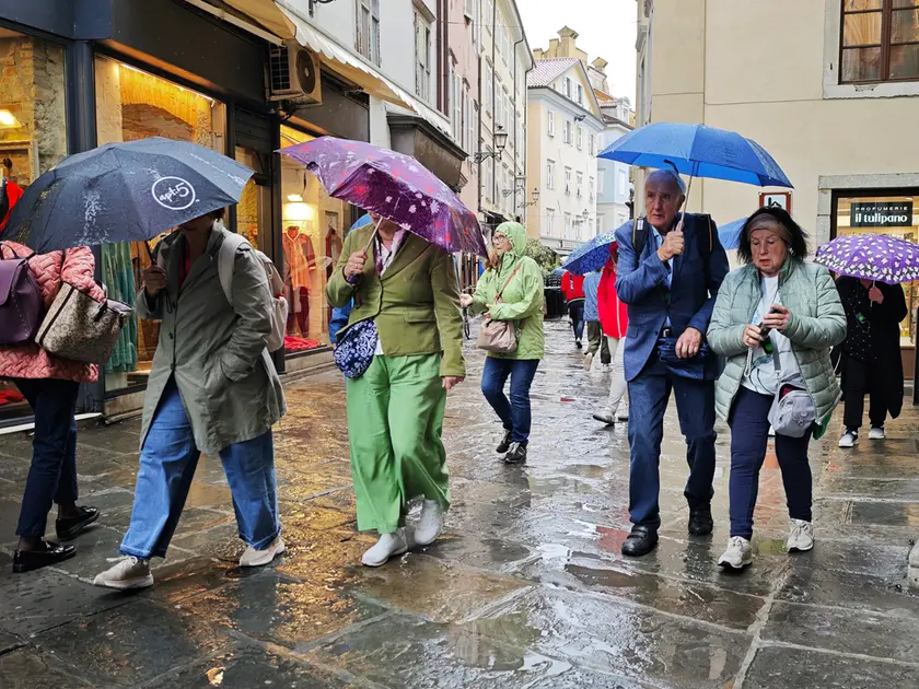 Un gruppo di turisti si ripara dalla pioggia in via San Sebastiano a Trieste (foto Andrea Lasorte)