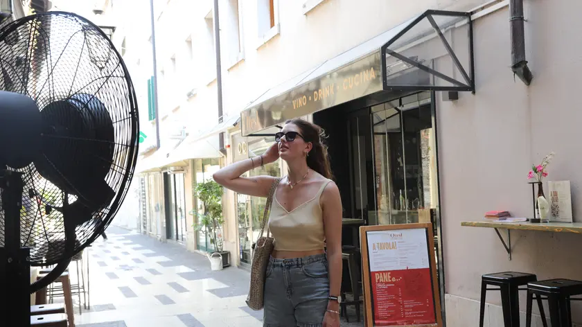 Una ragazza cerca refrigerio davanti a un maxi-ventilatore installato fuori da un locale pubblico