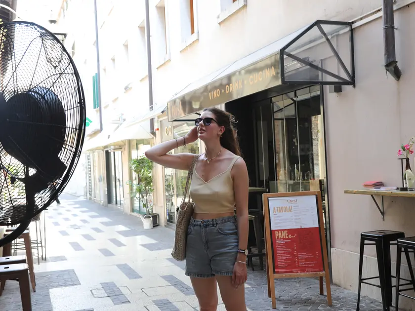 Una ragazza cerca refrigerio davanti a un maxi-ventilatore installato fuori da un locale pubblico
