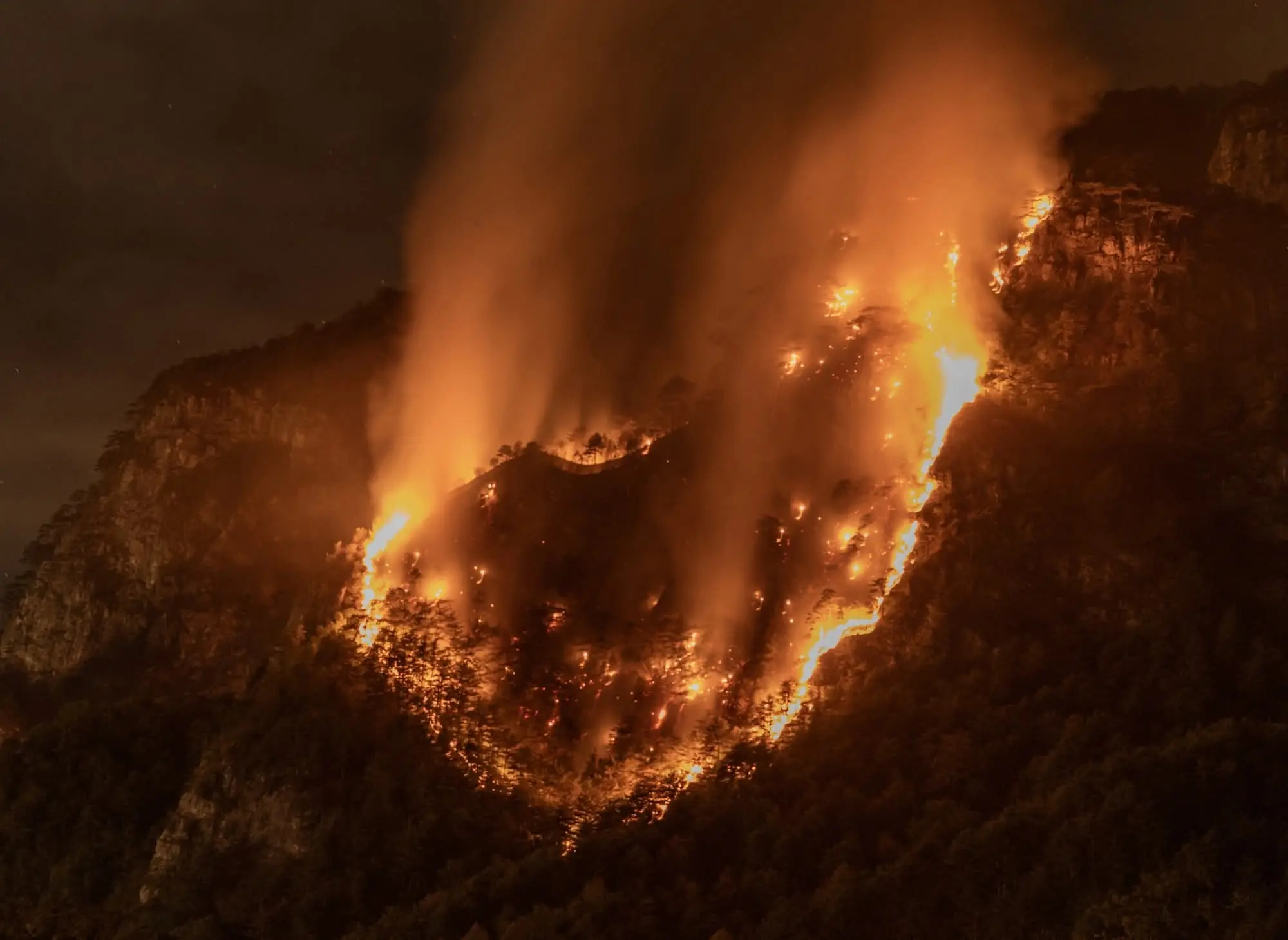 Le colonne di fumo degli incendi che stanno bruciando in Carnia sono visibili a chilometri di distanza e in alcune zone l’aria è diventata difficile da respirare. Una coltre grigia avvolge vallate e montagne, oscurando il cielo e cambiando il volto del paesaggio. Nella notte appena trascorsa, nel buio erano le fiamme sui versanti a illuminare la montagna, mentre con il giorno il fumo è tornato a dominare lo scenario.