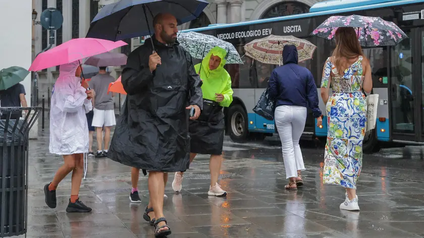 Alcuni passanti con ombrello e mantellina venerdì pomeriggio a Trieste (foto Andrea Lasorte)