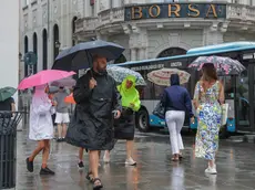 Alcuni passanti con ombrello e mantellina venerdì pomeriggio a Trieste (foto Andrea Lasorte)