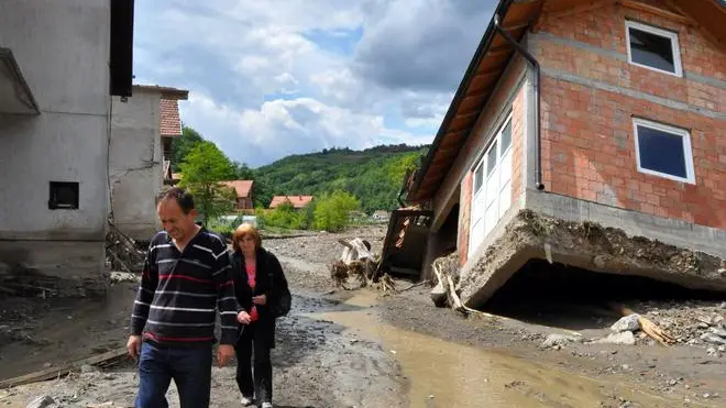 epa04213600 A picture made available 19 May 2014 shows people passing by damaged houses after flooding in Krupanj, 150 km southeast of Belgrade, Serbia, 18 May 2014. Clean-up began on 19 May after massive floods in parts of Serbia and Bosnia, even as cities on the river Sava braced for the arrival of a new wave of flooding. The situation was particularly grave in Krupanj, which has been without drinking water and electricity since 14 May, and Obrenovac, near Belgrade that saw the deaths of 12 people as flood waters covered most of the town. EPA/DRAGAN KARADAREVIC