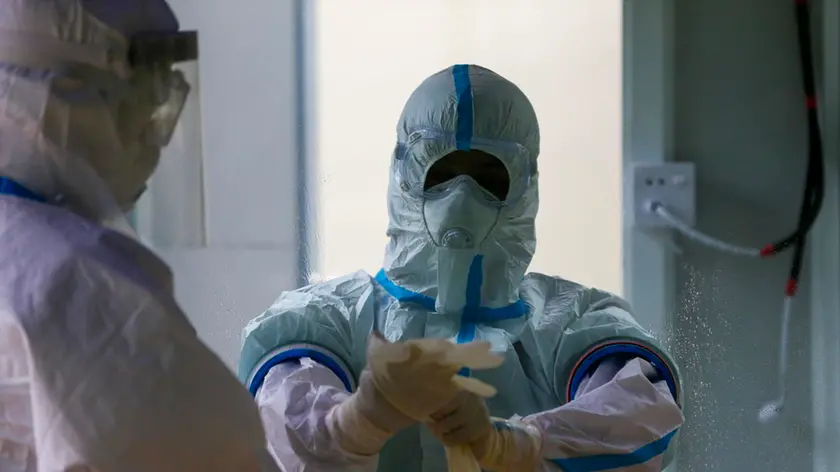 epa08596704 Medical worker wearing a full protective suit puts on new gloves at a swabbing booth during swab tests for COVID-19 in Yangon, Myanmar, 11 August 2020. Myanmar Football Federation started testing all professional soccer players, team members and referees for SARS-CoV-2 coronavirus, as the country is scheduled to restart the professional league. EPA/LYNN BO BO