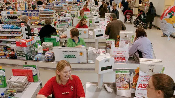 ca. 2004, York, North Yorkshire, England, UK --- Original caption: Smiling worker and a happy customer at the many tills of the Monks Cross ASDA. ASDA was formed by a group of farmers from Yorkshire and now has 265 stores and 19 depots across the UK. It was bought by Wal-Mart in 1999, and in 2004 was the UK's 2nd largest grocery chain. --- Image by © Gideon Mendel/Corbis