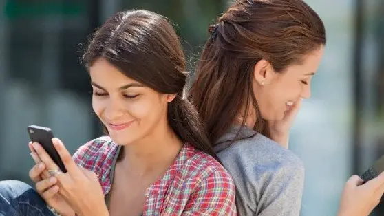 Two young women sitting back to back and text messaging --- Image by © Fabrice Lerouge/Onoky/Corbis