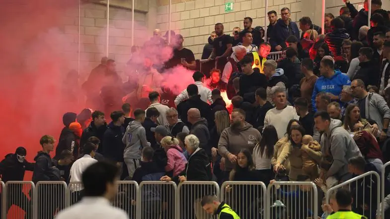 A destra una mamma tiene in braccio il suo neonato, a sinistra i disordini. Foto Tomaž Primožič Fpa