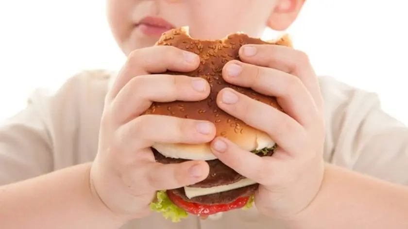 Un bambino divora un hamburger con salse e formaggio