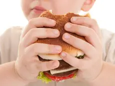 Un bambino divora un hamburger con salse e formaggio