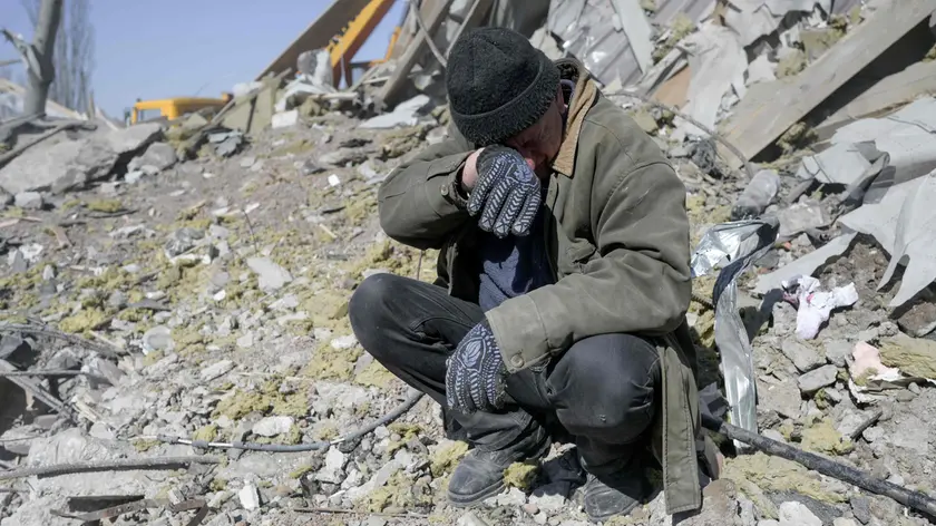 A man helps Ukrainian soldiers searching for bodies in the debris at the military school hit by Russian rockets the day before, in Mykolaiv, southern Ukraine, on March 19, 2022. - Ukrainian media reported that Russian forces had carried out a large-scale air strike on Mykolaiv, killing at least 40 Ukrainian soldiers at their brigade headquarters. (Photo by BULENT KILIC / AFP)