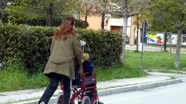 Una badante mentre porta a passeggio un anziano