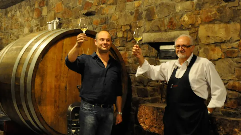 Beniamino Zidarich (a sinistra) con un bicchiere di vino nelle cantine dell'azienda a Prepotto