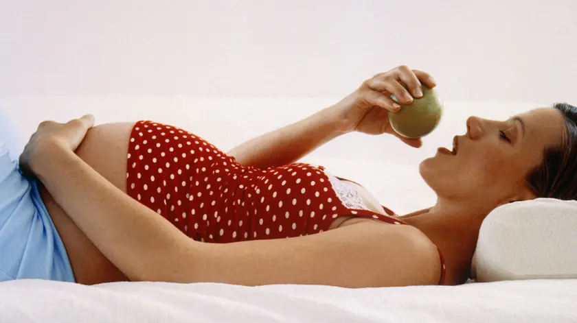 Pregnant Woman Eating Apple on Bed --- Image by © Holger Winkler/Corbis
