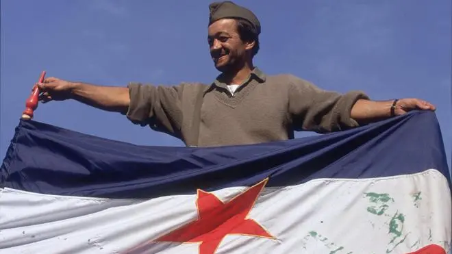 09 Oct 1991, Jasenovac, Croatia --- A soldier holds up the former Yugoslavian flag as the Yugoslavian Federal Army takes Jasenovac, a symbolic location and Croat stronghold, during the Yugoslavian Civil War. During World War II, Jasenovac was a concentration camp and the site of Serb massacres by fascist Ustashe Croats. Conflict between the Yugoslavian forces and the Croatian National Guard began after Croatia declared independence on June 25, 1991, beginning a civil war which dragged on for four years. --- Image by © Jacques Langevin/Sygma/Corbis