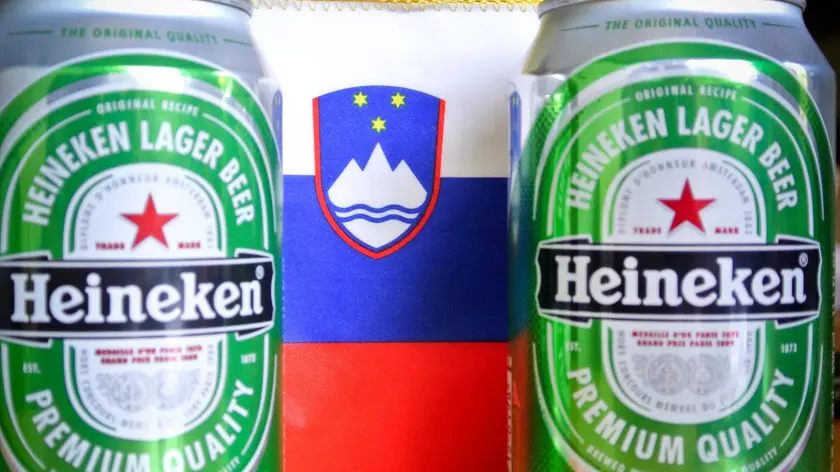 Le classiche lattine della birra Heineken davanti a una bandiera della Slovenia