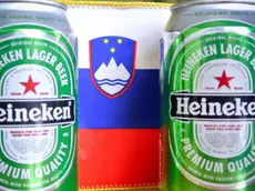 Le classiche lattine della birra Heineken davanti a una bandiera della Slovenia