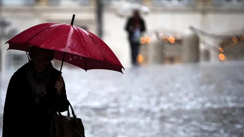 Una persona si ripara con l'ombrello sotto la pioggia in piazza Colonna a Roma, 15 dicembre 2017. ANSA/ANGELO CARCONI