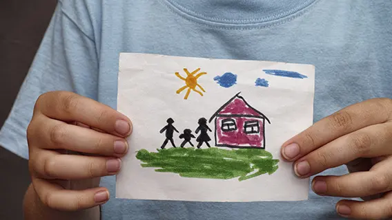 Child holds a drawn house with family. Close up.