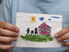 Child holds a drawn house with family. Close up.