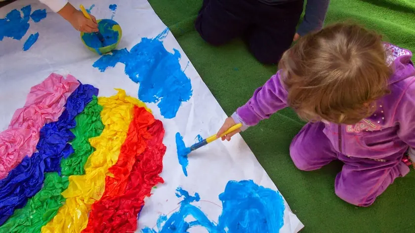 Una bambina intenta a disegnare un arcobaleno in una scuola dell’infanzia