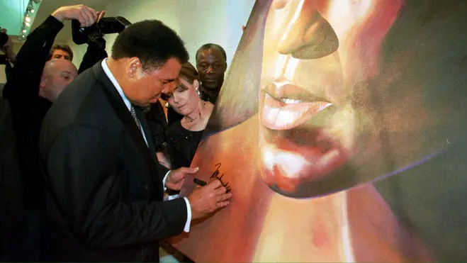 LAX99 - 19990310 - BEVERLY HILLS, CA, UNITED STATES : Muhammed Ali(L) signs a painting as its artist Caryn Fregoso(C) watches during an exhibition at the Very Special Arts Gallery West in Beverly Hills, CA 10 March 1999. Ali attended the exhibition "Strength of Greatness" at the gallery, which features works of art created by people suffering from Parkinson' Disease. The event raised money to create awareness and conduct research about the disease. EPA/ AFP PHOTO Frederick M. Brown