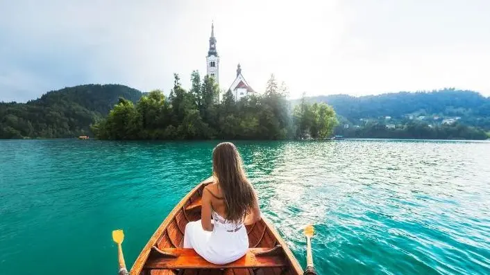 Una turista sulla caratteristica barchetta del lago di Bled ammira la chiesetta sull’isola. Bled è una delle località turistiche più gettonate