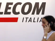 Una ragazza con un cellulare passa vicino ad un logo di Telecom in una foto d'archivio. ANSA / ETTORE FERRARI