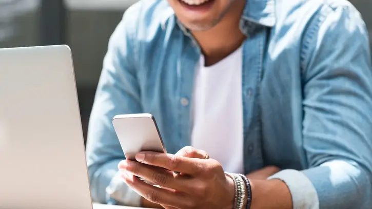 Close up of a student man using smart phone and laptop in cafe. Closeup of hand of a young man using smartphone. Happy african man reading a message phone outdoor.