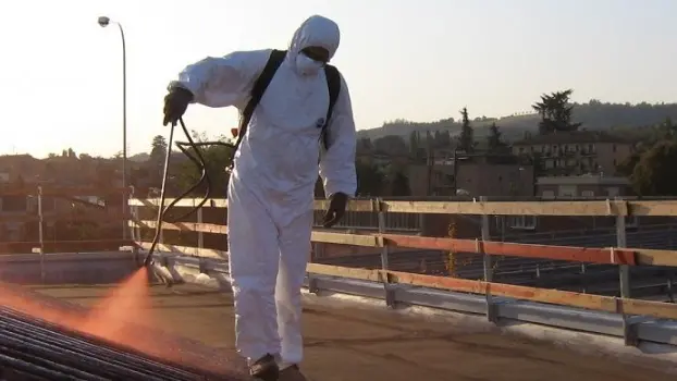 Un operaio a contatto con una tettoia di amianto protetto da tuta e maschera