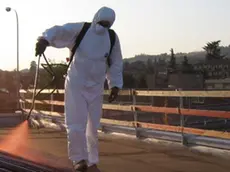 Un operaio a contatto con una tettoia di amianto protetto da tuta e maschera