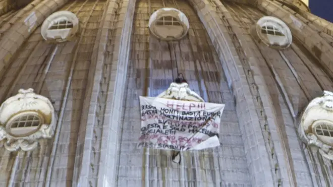 L'uomo arrampicatosi sulla cupola di San Pietro a Roma espone uno striscione in cui si legge "Basta Monti, basta Europa, basta multinazionali", 2 ottobre 2012. L'imprenditore triestino, Marcello Di Finizio, non nuovo a singolare iniziative di protesta, è appoggiato sulla finestra del cupolone. ANSA/MASSIMO PERCOSSI