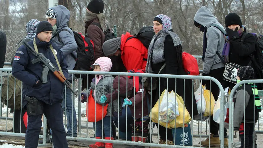 epa05109208 An armed official stands guard as migrants from Syria, Iraq and Afghanistan walk in very cold weather, through snow from Macedonia to a camp for the temporary acceptance of migrants in the village Miratovac, on the border between Serbia and Macedonia, near to the south Serbian city of Presevo, 18 January 2016. Since the second half of November 2015, countries further along the Balkan route - Macedonia, Serbia, Croatia, Slovenia and Austria have stopped all so-called economic migrants and are allowing only Syrians, Afghans and Iraqis to pass. EPA/DJORDJE SAVIC