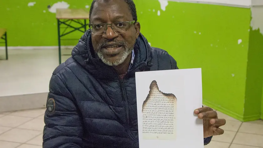 Bou Konate mostra la pagina bruciata del Corano ricevuta dal centro