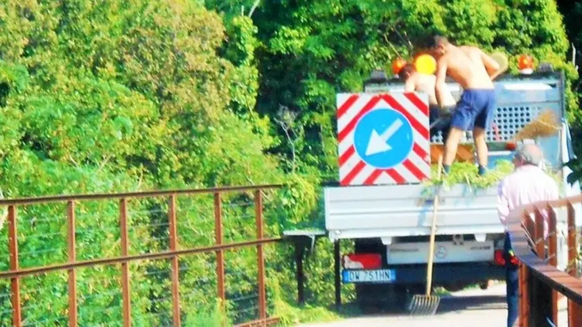 Dopo aver fatto pulizia sulla ciclabile, gli operai buttano giù dal ponte i rifiuti