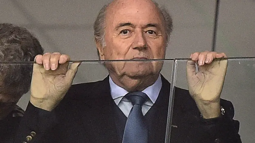 FIFA President Sepp Blatter peers over a barrier as he takes his seat for the group E World Cup soccer match between Honduras and Ecuador at the Arena da Baixada in Curitiba, Brazil, Friday, June 20, 2014. (AP Photo/Martin Meissner)