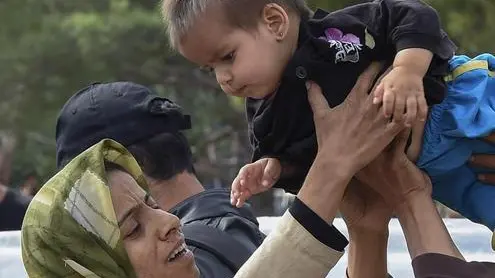 epaselect epa04892540 A mother is reunited with her child after they were separated a day before when migrants tried to break through a cordon of Macedonian special police forces to cross into Macedonia from Greece, near the southern city of Gevgelija, The Former Yugoslav Republic of Macedonia, 22 August 2015. Macedonian security forces strengthened the barricades along the Greek border 22 August, where thousands of refugees from the Middle East were stranded after a hot day and a rainy, chilly night, local media reported. EPA/GEORGI LICOVSKI