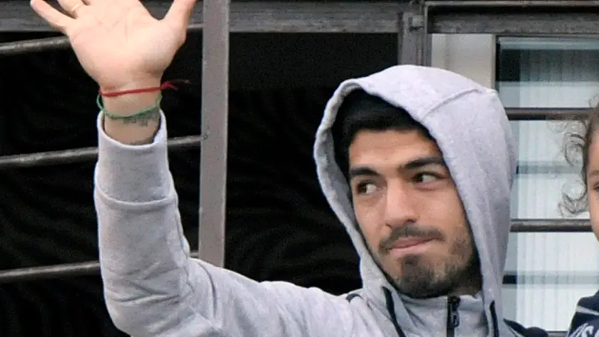 Uruguay's soccer player Luis Suarez holds his daughter as he greets fans from their home's balcony on the outskirts of Montevideo, Uruguay, Friday, June 27, 2014. Suarez returned to Montevideo early Friday, arriving too late to see the hundreds of Uruguay fans who had gathered the previous night to give him a hero's welcome despite his World Cup banishment. (AP Photo/Matilde Campodonico)