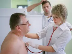 Doctor listening to patient's heart --- Image by © Mika/Corbis